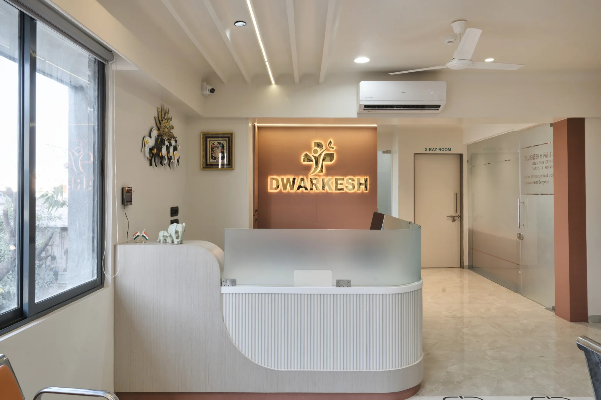 Modern white and wood-themed hospital reception desk and lobby interior design at Dwarkesh Hospital.